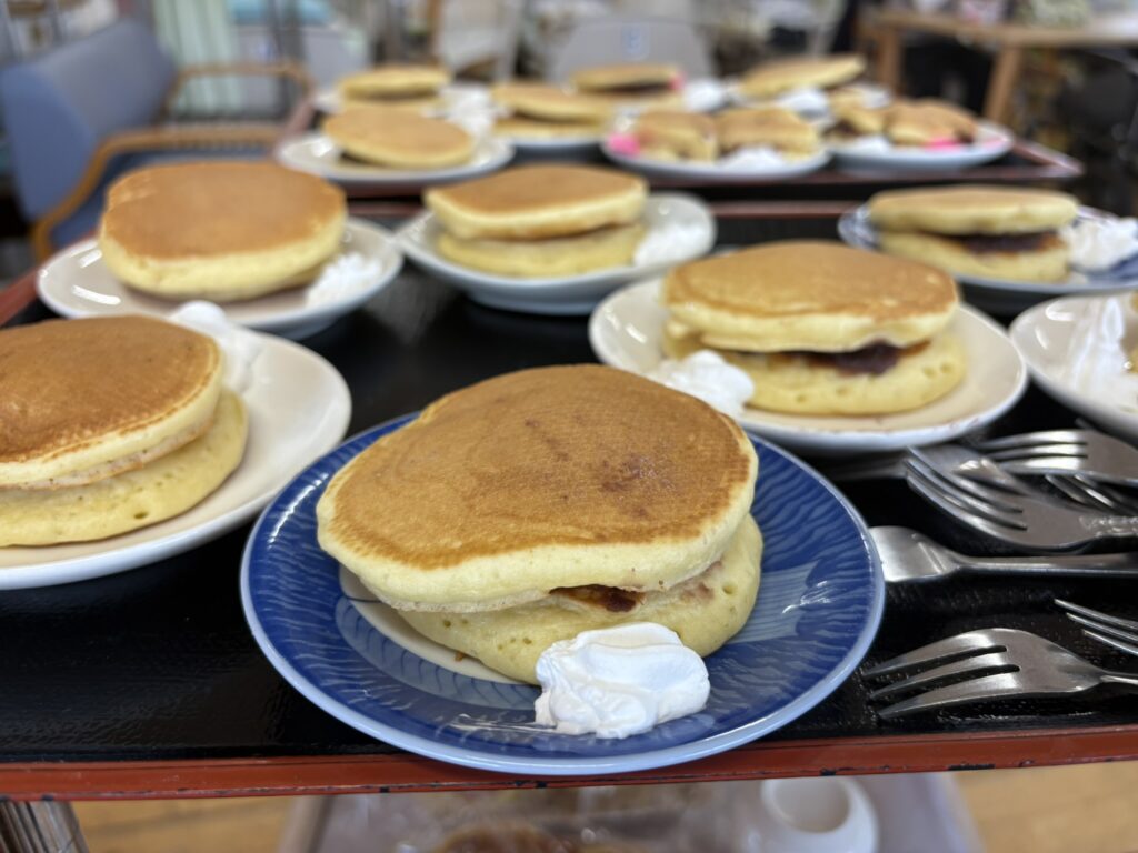 こんがりと黄金色に焼けたふっくらしたどら焼き。青い縁取りのお皿にのせられ、サイドには白いホイップクリームが添えられている。